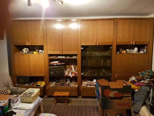 Großer Wohnzimmerschrank aus Holz mit Glastüren, Dekorationen und Umzugskartons im Raum.