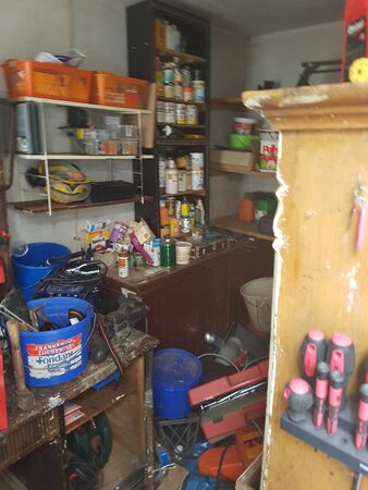 Werkstatt mit Regalen voller Werkzeug, Schraubenziehern, Farbeimern und Bastelmaterial.